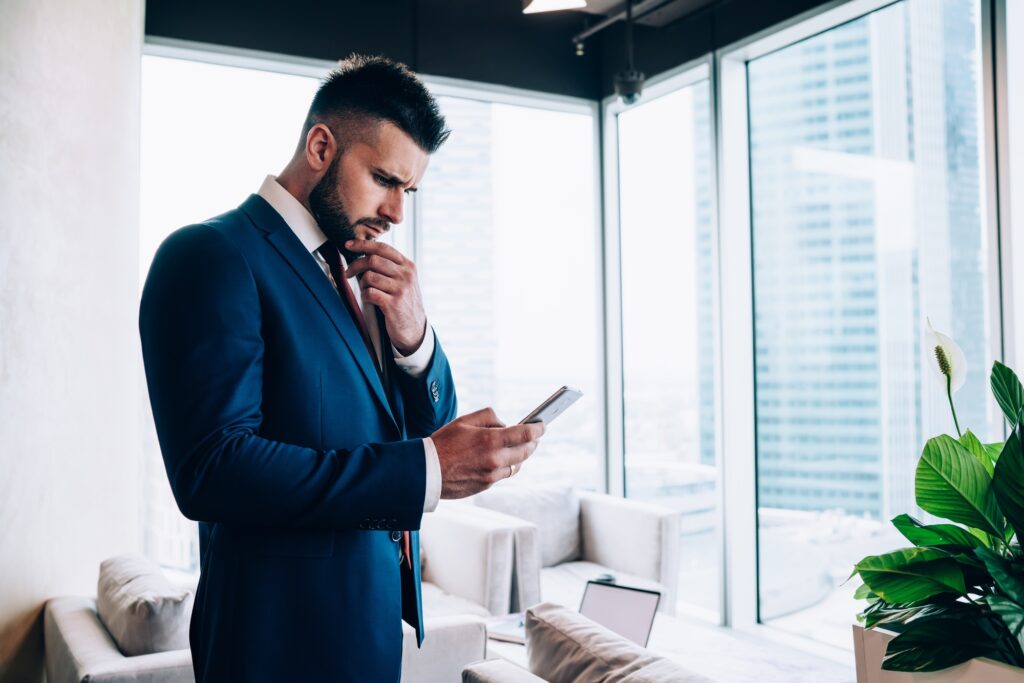 Concerned male manager in suit messaging on smartphone at office